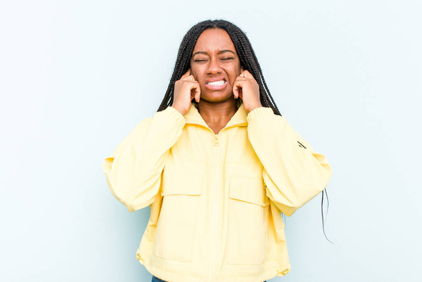 Молодая афроамериканка с косичками на синем фоне закрывает уши руками. - Фото, изображение