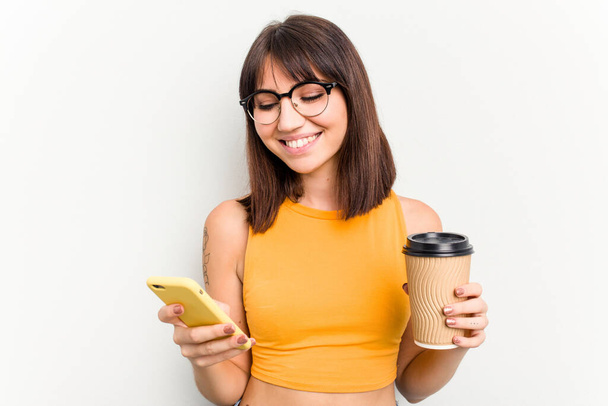 Young caucasian woman holding a take away coffee and a mobile phone isolated on white background - Fotografie, Obrázek