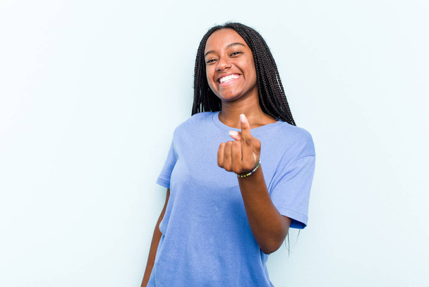 Jonge Afro-Amerikaanse vrouw met vlechten haar geïsoleerd op blauwe achtergrond wijzend met de vinger naar je alsof uitnodigen dichterbij komen. - Foto, afbeelding