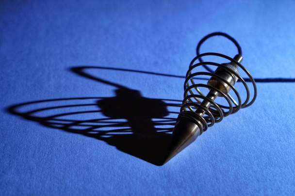 Metall-Wünschelrutenpendel und sein Schatten auf blauem Hintergrund. - Foto, Bild