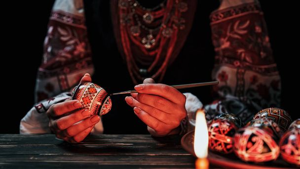 Ukrainian woman painting traditional ornamets on Easter egg - pysanka. Artist working in national costume under candle light. Preparation for Christian holiday. High quality  - Fotografie, Obrázek
