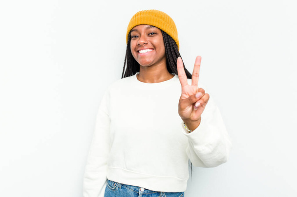 Giovane donna afroamericana isolata su sfondo bianco gioiosa e spensierata mostrando un simbolo di pace con le dita. - Foto, immagini