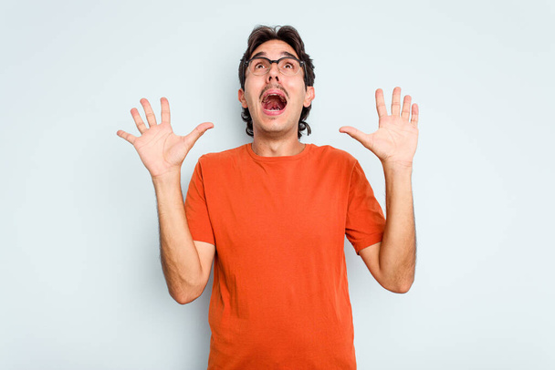 Young hispanic man isolated on blue background screaming to the sky, looking up, frustrated. - Foto, Imagen