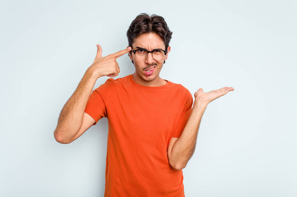 Young hispanic man isolated on blue background showing a disappointment gesture with forefinger. - Фото, изображение