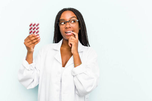 Young African American pharmacist woman isolated on blue background relaxed thinking about something looking at a copy space. - Photo, image