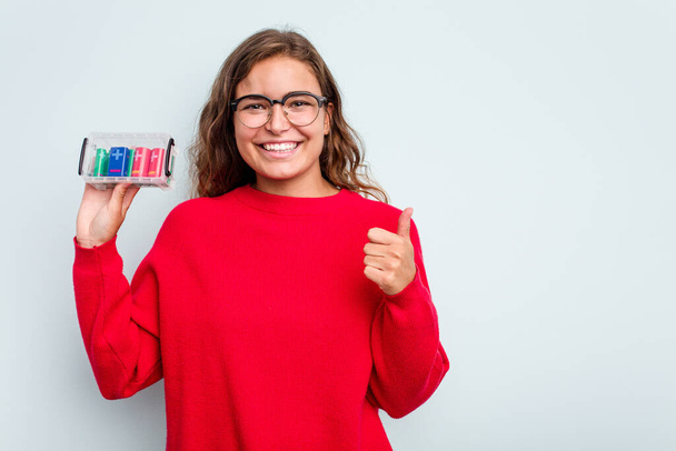 Young caucasian woman holding battery box isolated on blue background smiling and raising thumb up - Photo, Image