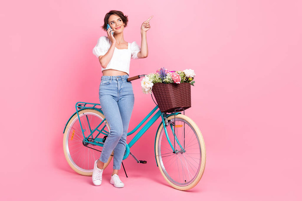 Full length photo of dreamy cute lady wear white crop top riding bike talking modern gadget empty space isolated pink color background. - Fotografie, Obrázek