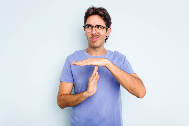 Young hispanic man isolated on blue background showing a timeout gesture. - Fotó, kép