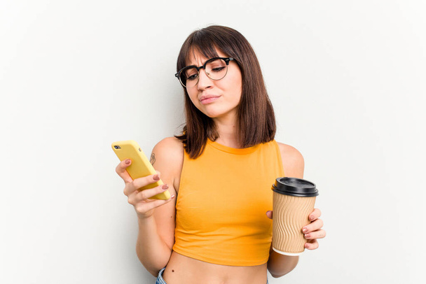Joven mujer caucásica sosteniendo un café para llevar y un teléfono móvil aislado sobre fondo blanco - Foto, Imagen