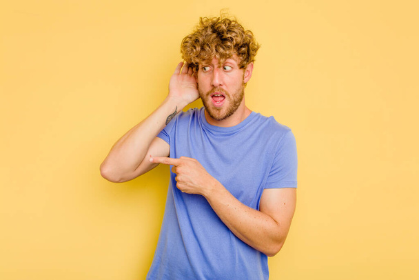 Young caucasian man isolated on yellow background trying to listening a gossip. - Photo, Image