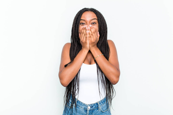 Joven mujer afroamericana aislada sobre fondo blanco riendo de algo, cubriendo la boca con las manos. - Foto, imagen