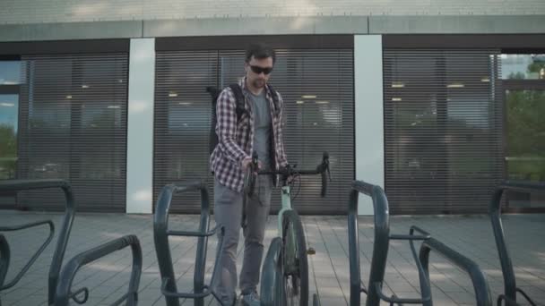 Bisikletçi Almanya 'da bisiklet parkına park eder ve bisikletini kilitler. Güvenlik ve ulaşım. Bisikleti park yerine kilitleyen adam. Bisiklet park alanındaki hırsızlık önleyici kilidi kapatmak için banliyö anahtarı kullan - Video, Çekim