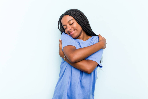 Young African American woman with braids hair isolated on blue background hugs, smiling carefree and happy. - Photo, Image