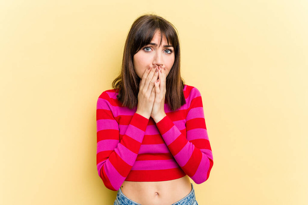 Jonge blanke vrouw geïsoleerd op gele achtergrond bedekken mond met handen kijken bezorgd. - Foto, afbeelding