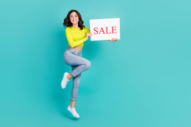 Full body portrait of cheerful lady hands hold paper sale banner jump isolated on teal color background. - Фото, изображение