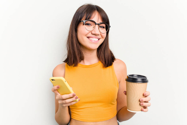 Joven mujer caucásica sosteniendo un café para llevar y un teléfono móvil aislado sobre fondo blanco - Foto, imagen