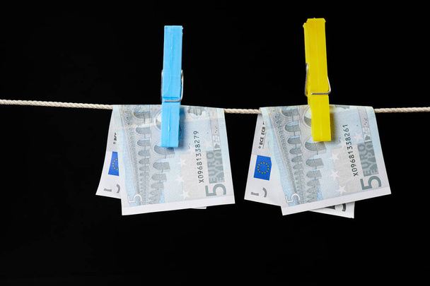 Cinco billetes en euros sujetados con pinzas de ropa se secan sobre un tendedero sobre fondo oscuro - Foto, Imagen