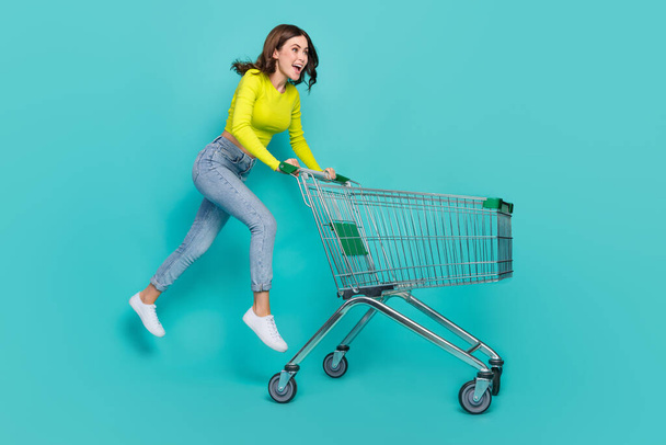 Full length photo of hooray brunette hair young lady go with trolley wear neon shirt jeans boots isolated on teal color background. - Fotoğraf, Görsel