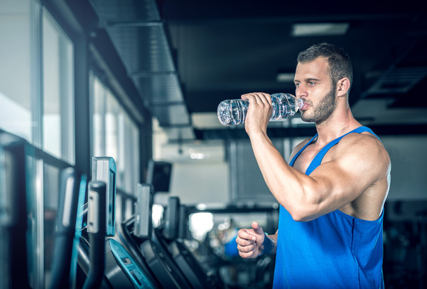 Young man drinking water in gym - Фото, изображение
