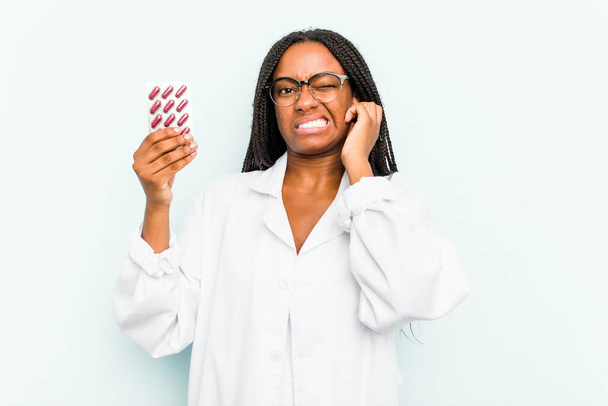 Young African American pharmacist woman isolated on blue background covering ears with hands. - Photo, Image