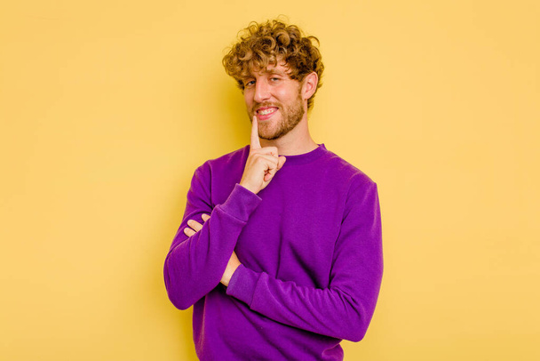 Young caucasian man isolated on yellow background smiling happy and confident, touching chin with hand. - Photo, Image