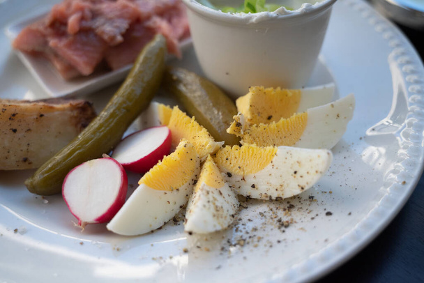 A plate of delicacies: pickled herring fish, baked potato, slices of hard-boiled egg, pickled cucumber and radish - Photo, Image