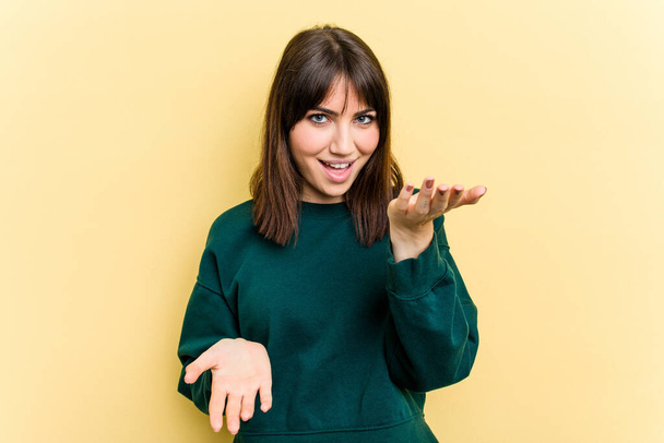 Young caucasian woman isolated on yellow background makes scale with arms, feels happy and confident. - Фото, изображение