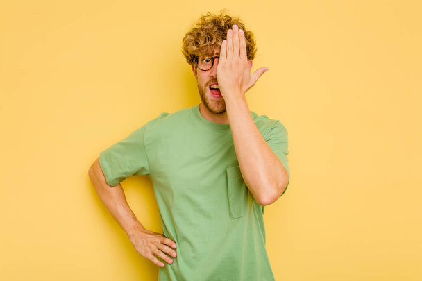 Young caucasian man isolated on yellow background having fun covering half of face with palm. - Photo, Image