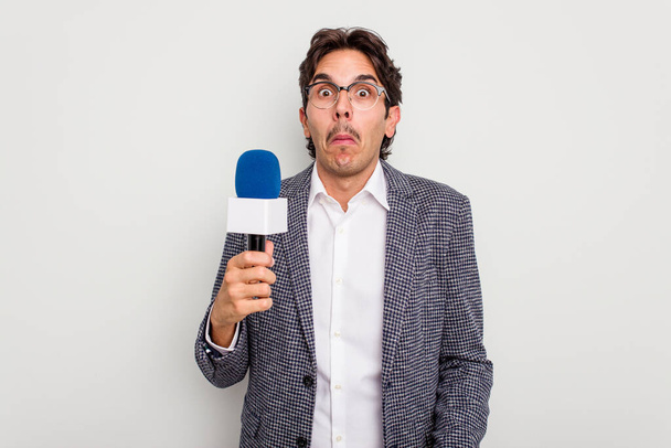 Young hispanic TV presenter man isolated on white background shrugs shoulders and open eyes confused. - Photo, Image
