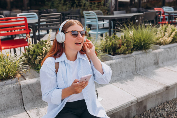 Close up portrait of a lovely happy young girl listening to music through wireless earphones on urban background. Music lover enjoying music. Lifestyle concept. - Фото, изображение