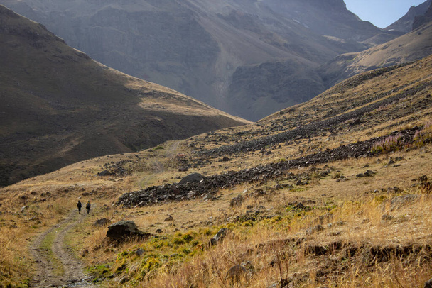 Οι άντρες περπατούν στα βουνά κατά μήκος ενός χωματόδρομου - Φωτογραφία, εικόνα