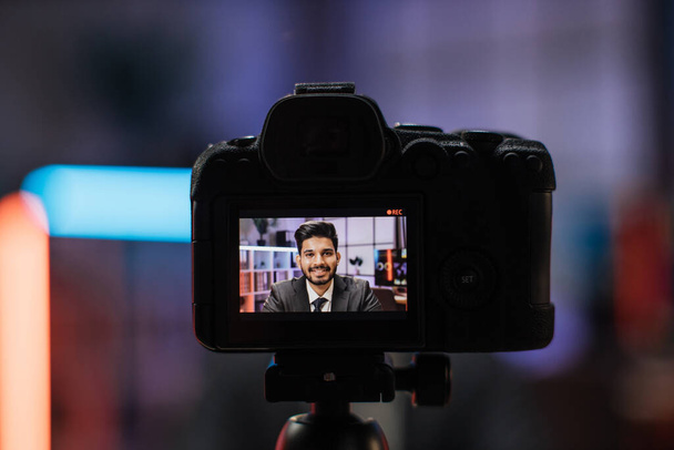 View from camera screen of attractive positive confident experienced smart indian bearded office manager recording video vlog for internet audience in evening office. - 写真・画像
