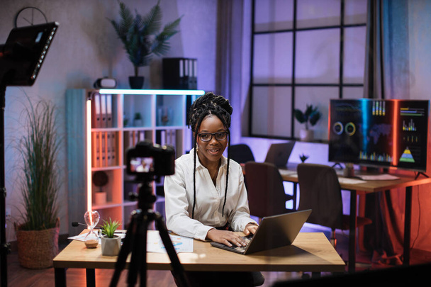 Positive attractive confident experienced smart african american businesswoman office manager recording video vlog for internet audience in evening office. - 写真・画像