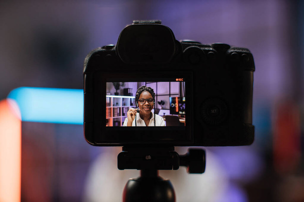 Focus on camera screen with attractive confident experienced smart female african american office manager in headset recording video vlog for internet audience in evening office. - Fotoğraf, Görsel