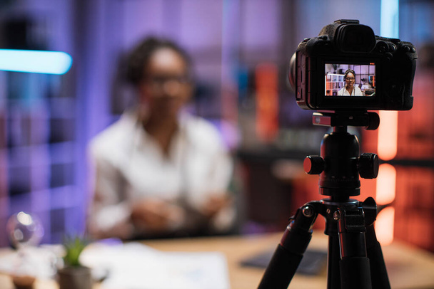 Focus on camera screen with attractive confident experienced smart female african american office manager recording video vlog for internet audience in evening office. - Fotó, kép