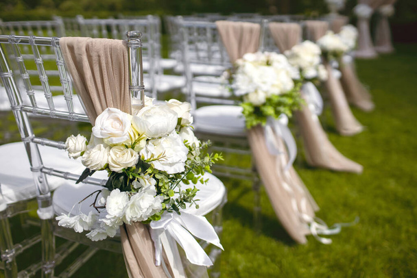 Hochzeitsdekor in Form von Blumen auf den Stühlen der Gäste für die Trauung. Vorbereitung für die Hochzeitszeremonie und schöne Dekoration. Blumen auf Stühlen aus nächster Nähe - Foto, Bild