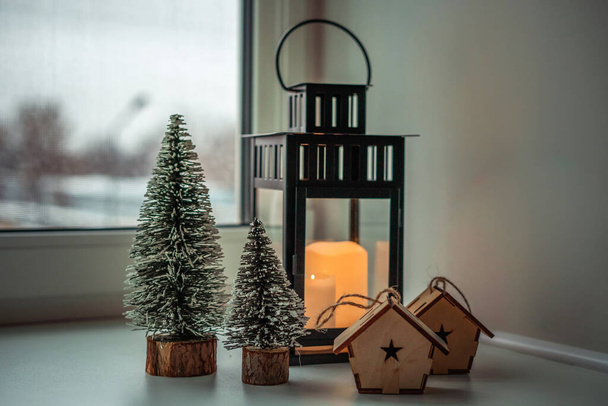 una araña grande con velas, árboles de Navidad y casas de madera en el alféizar de la ventana - Foto, imagen
