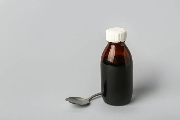 Пляшка сиропу і ложки кашлю на сірому фоні
 - Фото, зображення