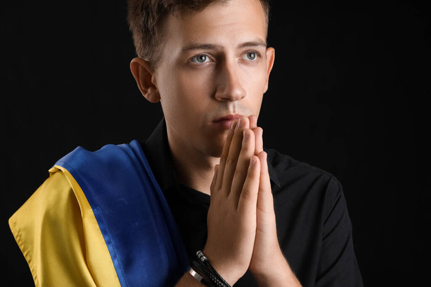 Joven con bandera de Ucrania rezando sobre fondo negro, primer plano - Foto, imagen