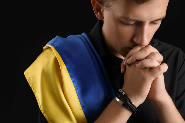 Jovem com bandeira da Ucrânia orando em fundo preto, close-up - Foto, Imagem