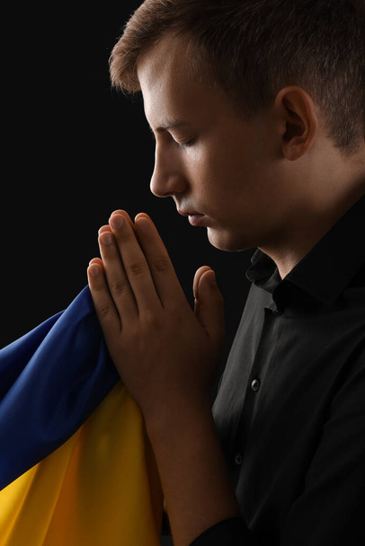 Joven con bandera de Ucrania rezando sobre fondo negro, primer plano - Foto, imagen