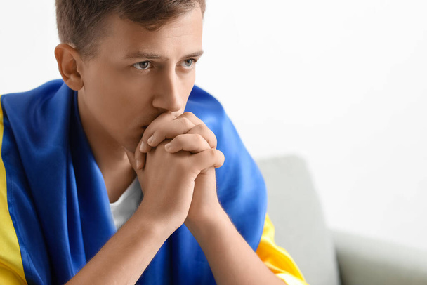 Young man with flag of Ukraine praying at home, closeup - Photo, Image