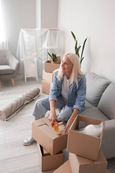 Mulher madura gravando caixa de papelão na sala de estar no dia em movimento - Foto, Imagem