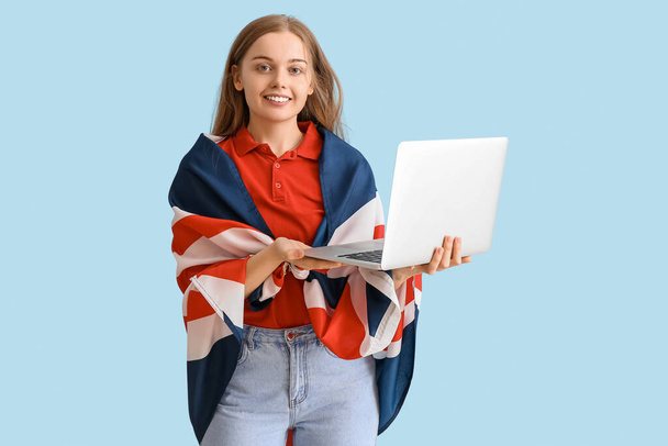 Young woman with UK flag using laptop on blue background - Foto, afbeelding