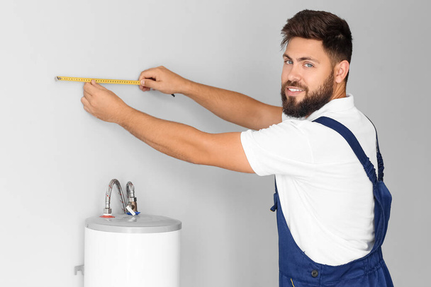 Male plumber measuring wall before installing boiler in bathroom - Photo, Image