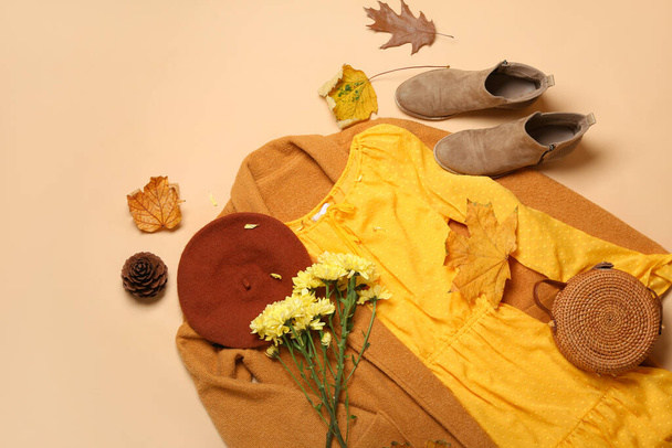Stylish female clothes, bouquet of flowers and autumn leaves on beige background - Foto, Bild