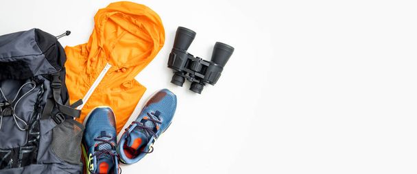Binoculars, tourist backpack, raincoat, shoes on a white background. Top view, flat lay. Banner. - Photo, Image