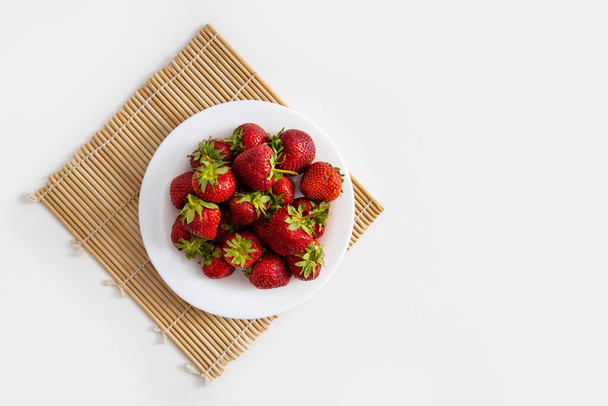 Witte plaat met aardbeien op een witte tafelondergrond. Bovenaanzicht, vlak lay. - Foto, afbeelding