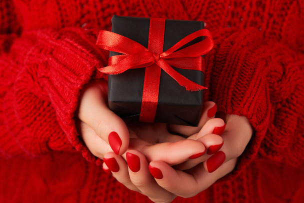 Manicured womans hands in red sweater holding gift box. Template for christmas valentines day sale. - Photo, Image