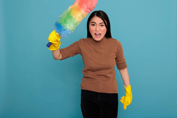 Ασιατική θυμωμένος ενεργητικός και την εμπιστοσύνη οικιακή εργάτης από την εργασία κρατώντας πολύχρωμο πινέλο σκόνης σε κίτρινα γάντια, Καθαρισμός έννοια σπίτι, Νοικοκυρά αισθάνονται απογοητευμένοι και αρνητικοί από τις καθημερινές δουλειές - Φωτογραφία, εικόνα